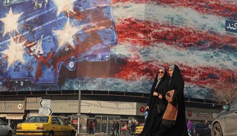TOPSHOT - Iranian women walk past an anti-US billboard installed on a building at the Enqelab Square in Tehran on January 26, 2026. (Photo by ATTA KENARE/AFP)