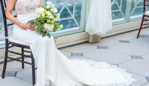 A gorgeous bride with a luxury wedding dress sitting on a chair holding a bridal bouquetSalon vjenčanica naplaćuje razgledavanje freepik