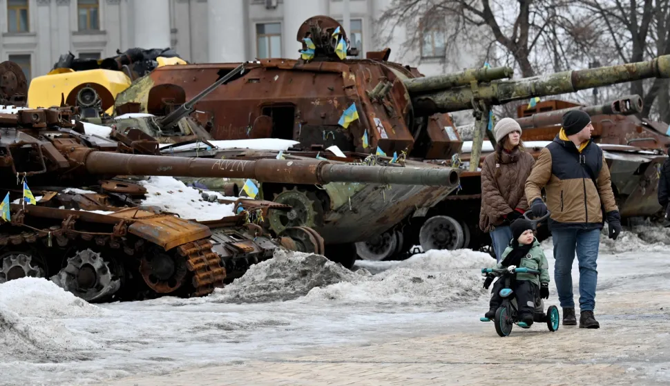 A couple and a boy on a bicycle walk in the open air exhibition of destroyed Russian military equipment in Kyiv on February 15, 2026, amid Russian invasion in Ukraine. (Photo by Sergei SUPINSKY/AFP)