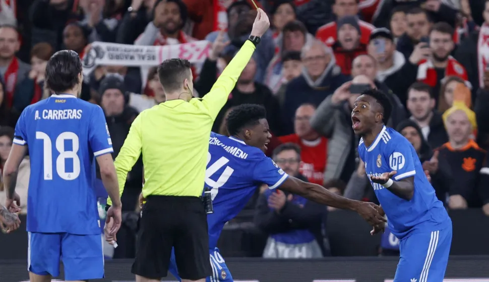 French referee Francois Letexier shows a yellow card to Real Madrid's Brazilian forward #07 Vinicius Junior as he celebrates scoring his team's first goal during the UEFA Champions League knockout round play-off first leg football match between SL Benfica and Real Madrid CF at Estadio da Luz in Lisbon on February 17, 2026. (Photo by FILIPE AMORIM/AFP)