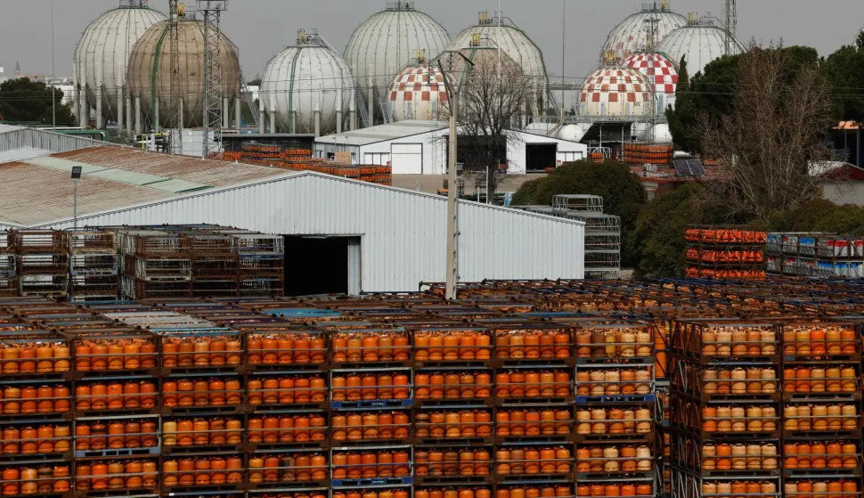Gas bottles are seen near storage tanks at a Liquefied Petroleum Gas (LPG) factory in Pinto, near Madrid, on March 5, 2026. Markets have been roiled much of the week as the conflict between the United States and Iran effectively closed shipping through the Strait of Hormuz, where a fifth of the world's crude oil travels as well as considerable liquefied natural gas (LNG) supplies travel through. (Photo by Oscar DEL POZO/AFP)