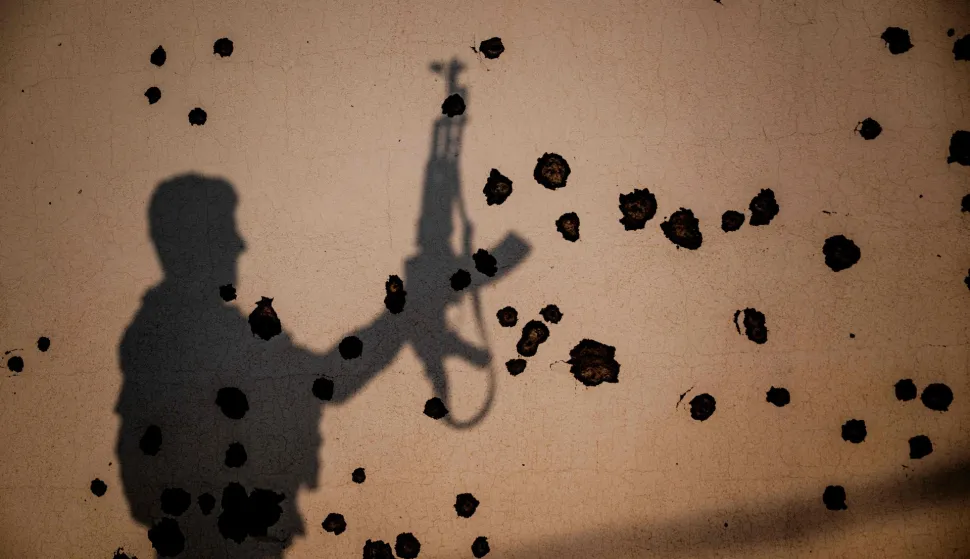 TOPSHOT - The shadow of a Kurdish fighter, a member of The Organization of Iranian Kurdistan Struggle (Sazmani Khabat), falls on the shrapnel scarred wall of a damaged building, following an Iranian drone attack to their base near Erbil, in Iraq's northern autonomous Kurdish region on March 9, 2026. Iran has designated Kurdish rebels groups as terrorist organisations, and many have previously fought its security forces in Kurdish-majority areas along the border. (Photo by Ozan KOSE/AFP)