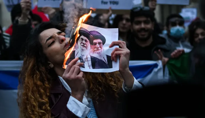 An anti-Iranian regime protester lights a cigarette with a lit paper depicting Ali Khamenei, Supreme Leader of Iran during a gathering outside the US Consulate in Milan, on January 13, 2026. (Photo by Piero CRUCIATTI/AFP)