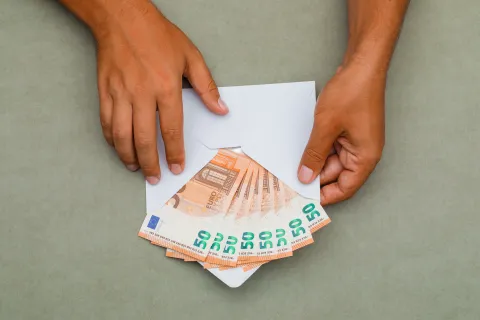 Financial concept on greenish grey background flat lay. man holding envelope full of banknotes. 