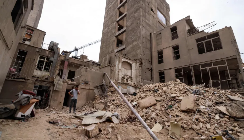 An Iranian man speaks on his mobile phone as he stands on the debris in front of destroyed buildings following a military strike on the Iranian capital Tehran on March 15, 2026. Iran's Foreign Minister said in an interview published on March 15, that the war pitting his country against the United States and Israel will only end when Tehran can be certain it will not be restarted. On February 28, Israel and the United States launched strikes on Iran, killing its supreme leader Ayatollah and triggering a war that spread across the Middle East. (Photo by Atta KENARE/AFP)/