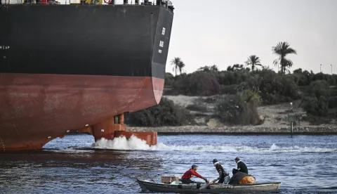 epa12547633 Men on a small boat sail near a ship crossing the Suez Canal towards the Mediterranean sea in Ismailia, Egypt, 25 November 2025. Danish shipping and logistics company Maersk will resume navigation of container ships through the Suez Canal in early December as the company plans full resumption of operations through the waterway, the Suez Canal authority said in a statement on 25 November. Maersk has been diverting container vessels away from the Suez Canal since January 2024 due to attacks carried out by Yemen's Houthi militants on commercial ships in the Red Sea and Gulf of Aden. EPA/MOHAMED HOSSAM