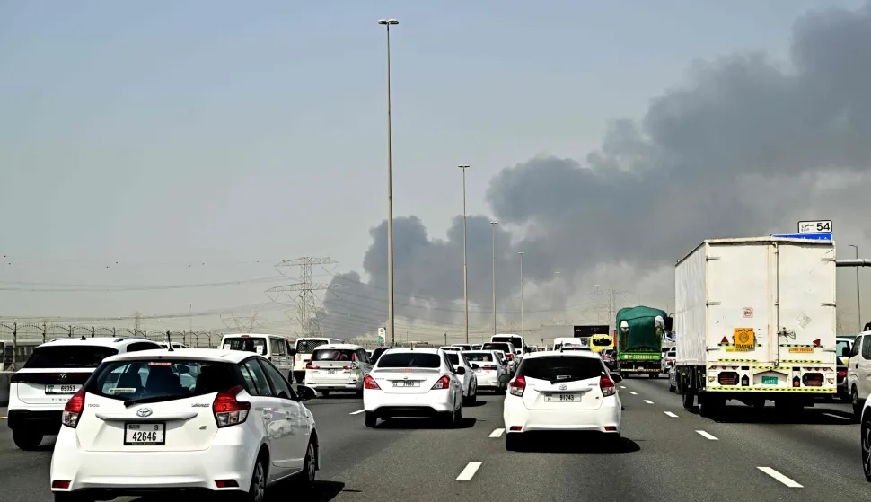 Smoke billows from an ongoing fire near Dubai International Airport as vehicles drive on a highway in Dubai on March 16, 2026. Flights were gradually resuming at Dubai airport on March 16, previously the world's busiest for international flights, the airport operator said, after a "drone-related incident" sparked a fuel tank fire nearby, as Iran kept up its Gulf attacks. (Photo by AFP)/