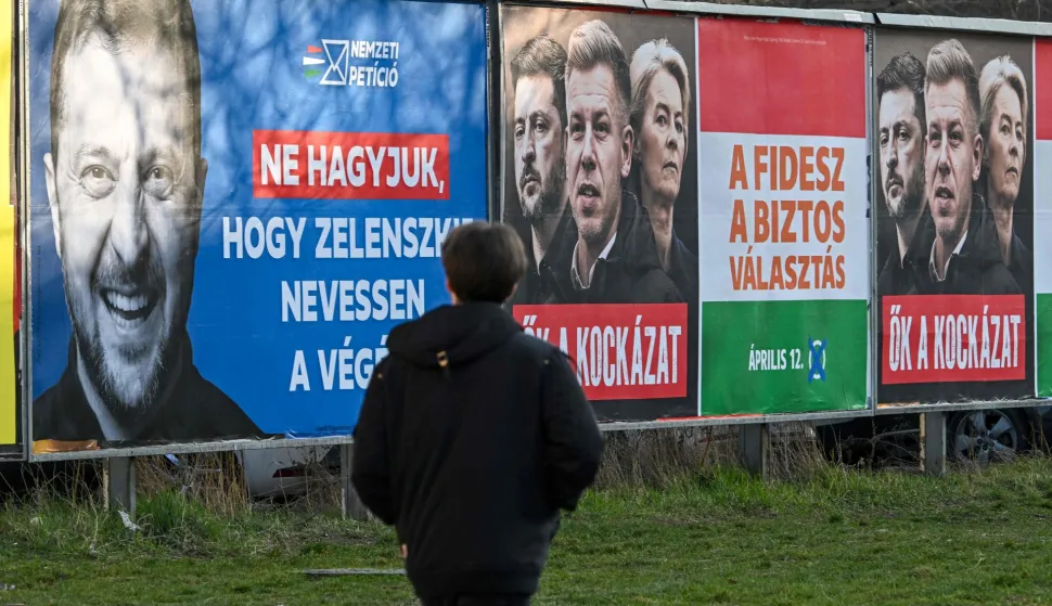 (FILES) A woman walks past a pro-government billboard featuring a portrait of Ukrainian President Volodymyr Zelensky (L), with the lettering reading, 'Let's not let Zelensky have the last laugh', and another billboard featuring European Commission President Ursula von der Leyen (R), Ukraine's President Volodymyr Zelensky (C), and Hungarian opposition leader Peter Magyar (L) with the lettering reading 'They themselves are the risk' in Budapest's 3rd district on March 3, 2026, in prepatation for the upcomping general election set to take place on April 12, 2026. Hungary's long-time premier Viktor Orban and his main opponent Peter Magyar are set to stage rival marches in Budapest on Sunday, March 15, 2026, both pushing allegations of foreign interference four weeks before the elections. (Photo by Attila KISBENEDEK/AFP)