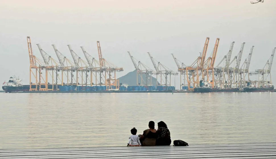 (FILES) A family sits against the backdrop of a dockyard off coast city of Fujairah, in the Strait of Hormuz in the northern Emirate on February 25, 2026. The US president sent a peace plan to Iran as he voiced optimism on March 25, 2026 at ending nearly a month of warfare, with Tehran announcing that it will let "non-hostile" oil vessels go through the crucial Strait of Hormuz. Oil prices dropped sharply and stocks in Asia rose on broader de-escalation hopes following nearly four weeks of war, as the US president appeared to be ramping up efforts to bring an end to his joint military operation with Israel. (Photo by Giuseppe CACACE/AFP)