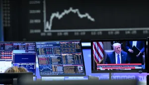 03 April 2025, Hesse, Frankfurt/Main: Behind a television monitor showing US President Donald Trump, the display board with the Dax curve shows falling share prices. The tariff package announced by US President Trump has pushed share prices sharply into the red. Photo: Arne Dedert/dpa Photo: Arne Dedert/DPA