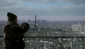 A woman looks out towards the Eiffel Tower and skyline of Paris from the observation gallery on the top of the Tour Montparnasse (Montparnasse Tower), in Paris on March 30, 2026. The Montparnasse Tower will close to the public on March 31, 2026 for five years for a major renovation program aimed at completely transforming the building and its surroundings. (Photo by Alain JOCARD/AFP)