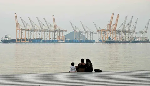 (FILES) A family sits against the backdrop of a dockyard off coast city of Fujairah, in the Strait of Hormuz in the northern Emirate on February 25, 2026. The US president sent a peace plan to Iran as he voiced optimism on March 25, 2026 at ending nearly a month of warfare, with Tehran announcing that it will let "non-hostile" oil vessels go through the crucial Strait of Hormuz. Oil prices dropped sharply and stocks in Asia rose on broader de-escalation hopes following nearly four weeks of war, as the US president appeared to be ramping up efforts to bring an end to his joint military operation with Israel. (Photo by Giuseppe CACACE/AFP)