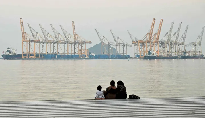 (FILES) A family sits against the backdrop of a dockyard off coast city of Fujairah, in the Strait of Hormuz in the northern Emirate on February 25, 2026. The US president sent a peace plan to Iran as he voiced optimism on March 25, 2026 at ending nearly a month of warfare, with Tehran announcing that it will let "non-hostile" oil vessels go through the crucial Strait of Hormuz. Oil prices dropped sharply and stocks in Asia rose on broader de-escalation hopes following nearly four weeks of war, as the US president appeared to be ramping up efforts to bring an end to his joint military operation with Israel. (Photo by Giuseppe CACACE/AFP)