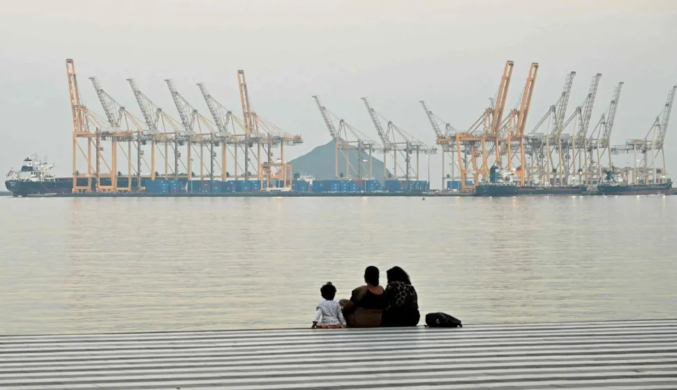 (FILES) A family sits against the backdrop of a dockyard off coast city of Fujairah, in the Strait of Hormuz in the northern Emirate on February 25, 2026. The US president sent a peace plan to Iran as he voiced optimism on March 25, 2026 at ending nearly a month of warfare, with Tehran announcing that it will let "non-hostile" oil vessels go through the crucial Strait of Hormuz. Oil prices dropped sharply and stocks in Asia rose on broader de-escalation hopes following nearly four weeks of war, as the US president appeared to be ramping up efforts to bring an end to his joint military operation with Israel. (Photo by Giuseppe CACACE/AFP)