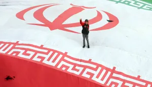 TOPSHOT - A boy raises his fist while standing on a giant Iranian flag during the funeral of Alireza Tangsiri, commander of the Iranian Revolutionary Guards' navy, alongside others killed in US-Israeli strikes on Iran at Enghelab Square in Tehran on April 1, 2026. Iran confirmed on March 30 that an Israeli strike had killed the commander of the naval force of the Revolutionary Guards, who Israel had said was responsible for the blocking of the Strait of Hormuz. A statement carried by the Guards' Sepah News website said Alireza Tangsiri "succumbed to severe injuries" from the attack last week. (Photo by AFP)/ALTERNATIVE CROP