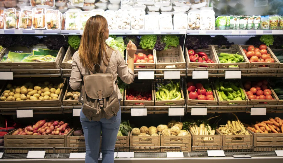 Good looking woman standing in front of vegetable shelves choosing what to buy.trgovina kupnja voće povrće