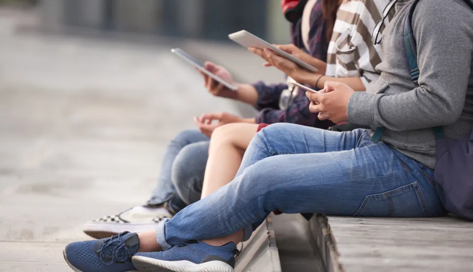 Close-up shot of unrecognizable friends gathered together outdoors and browsing Internet with help of devices, blurred backgroundmladi internet laptop djeca cyber sigurnost ilustracija freepik