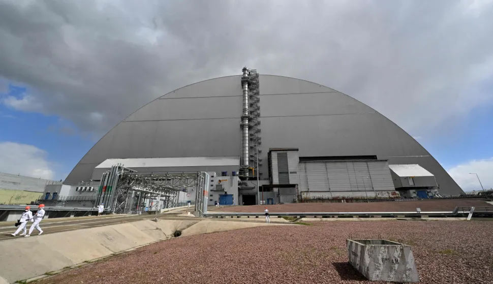 Employees walk in front of New Safe Confinement (NSC), covering the destroyed fourth reactor at the Chernobyl Nuclear Power Plant on April 23, 2026. Ukraine will on April 26, 2026 mark the 40th anniversary of the Chernobyl accident, the worst civilian nuclear disaster in history. The risks of new radioactive releases still remain today, as the site is threatened by Russian strikes after it invaded the neighbour four years ago. (Photo by Sergei SUPINSKY/AFP)