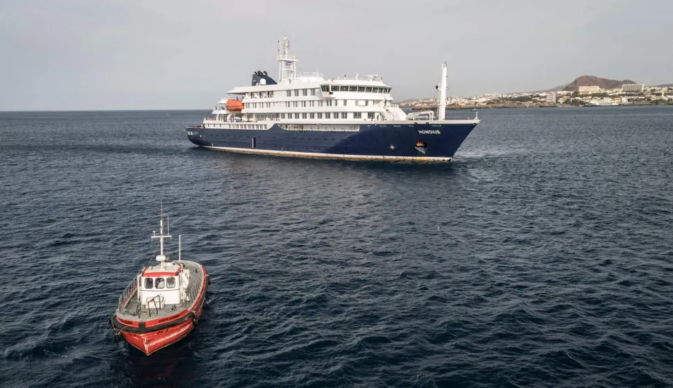This aerial view shows a boat heading towards the port from the cruise ship MV Hondius, stationary off the port of Praia, the capital of Cape Verde, on May 6, 2026. Evacuations were taking place on May 6, 2026 from a cruise ship stricken with a deadly outbreak of hantavirus, the World Health Organization said, as experts confirmed a rare strain that can be transmitted between humans.Three people, two crew members and one other person, thought to be infected with the virus were being taken off the MV Hondius, anchored off Cape Verde, the WHO said. (Photo by AFP)