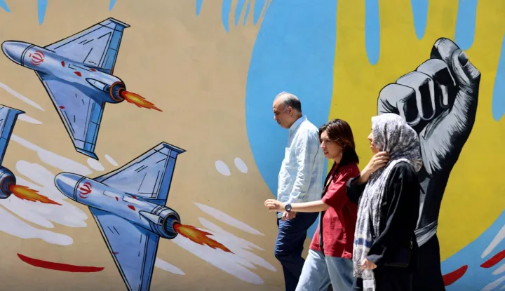 Iranians walk past an anti-US and anti-Israel mural painted on a wall in the capital Tehran on May 10, 2026. The spokesman for the Iranian parliament's national security commission warned the United States on May 10, against any attacks on vessels in Gulf waters, saying Iran's restraint was over. (Photo by ATTA KENARE/AFP)/