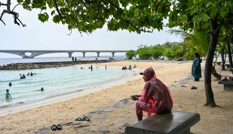 A man sits under a tree as it rains at Artificial Beach in Mal? on May 15, 2026. Rescue teams in the Indian Ocean archipelago of the Maldives searched for a second day on May 15 for the bodies of four missing Italians following the country's deadliest diving accident, officials said. (Photo by Mohamed Afrah/AFP)