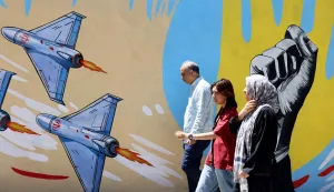 Iranians walk past an anti-US and anti-Israel mural painted on a wall in the capital Tehran on May 10, 2026. The spokesman for the Iranian parliament's national security commission warned the United States on May 10, against any attacks on vessels in Gulf waters, saying Iran's restraint was over. (Photo by ATTA KENARE/AFP)/