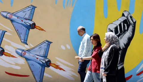 Iranians walk past an anti-US and anti-Israel mural painted on a wall in the capital Tehran on May 10, 2026. The spokesman for the Iranian parliament's national security commission warned the United States on May 10, against any attacks on vessels in Gulf waters, saying Iran's restraint was over. (Photo by ATTA KENARE/AFP)/