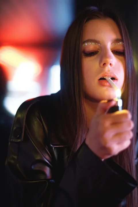 Fashion portrait of beautiful girl posing, dancing in colorful bright neon red lights. Model wearing trendy leather jacket and bright make up. Woman smoking sigarettes.cigarete pu&scaron;enje ilustracija