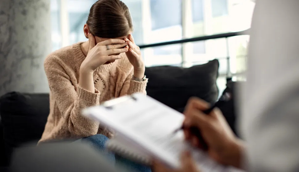 Sad woman holding her head in pain while having a meeting with psychotherapist.