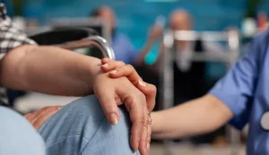 Social assistant worker consoling handicapped pensioner patient touching hands during homecare service. Healthcare support assistance. Social services nursing at home. Caregiver nurseumirovljenik zdravlje medicina starost bolest ilustracija