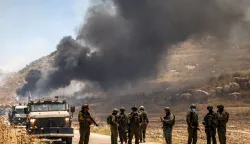 Israeli security forces stand guard along a road while behind smoke billows from an area reportedly set ablaze by Israeli settlers in the Palestinian village of Idna, west of Hebron in the occupied West Bank, on June 5, 2026. (Photo by HAZEM BADER/AFP)