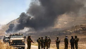 Israeli security forces stand guard along a road while behind smoke billows from an area reportedly set ablaze by Israeli settlers in the Palestinian village of Idna, west of Hebron in the occupied West Bank, on June 5, 2026. (Photo by HAZEM BADER/AFP)