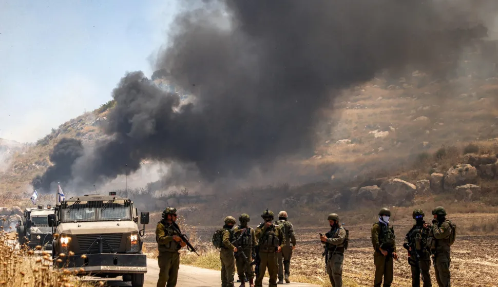 Israeli security forces stand guard along a road while behind smoke billows from an area reportedly set ablaze by Israeli settlers in the Palestinian village of Idna, west of Hebron in the occupied West Bank, on June 5, 2026. (Photo by HAZEM BADER/AFP)