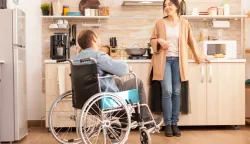 Disabled man sitting in chair and talking with wife while preparing meal. Disabled paralyzed handicapped man with walking disability integrating after an accident.