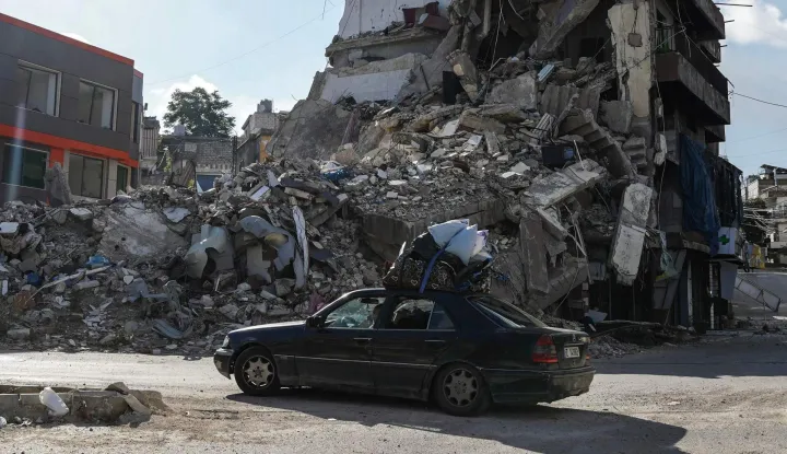 TOPSHOT - A car loaded with belongings drives past a destroyed building in Nabatieh on June 15, 2026. The United States and Iran said they reached a deal to end the Middle East war on all fronts including Lebanon, and reopen the vital Strait of Hormuz, but offered little indication on the thorny question of Tehran's nuclear programme. Washington and Islamabad said the agreement was to be signed on June 19 in Switzerland, signalling what would be a major breakthrough to ending months of war that have taken thousands of lives and roiled energy markets. (Photo by Abbas FAKIH/AFP)/ALTERNATIVE CROP