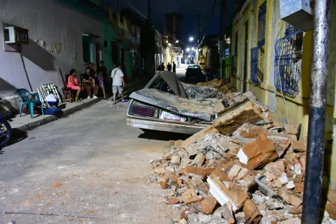 People gather on a street next to a damaged car and building following an earthquake in Valencia, Venezuela on June 24, 2026. Two earthquakes of magnitude 7.2 and 7.5 struck the same area of Venezuela on the evening of June 24, causing buildings to collapse, according to the United States Geological Survey (USGS) and AFP journalists. The quakes drove residents of the capital, Caracas, into the streets. (Photo by Jacinto OLIVEROS/AFP)