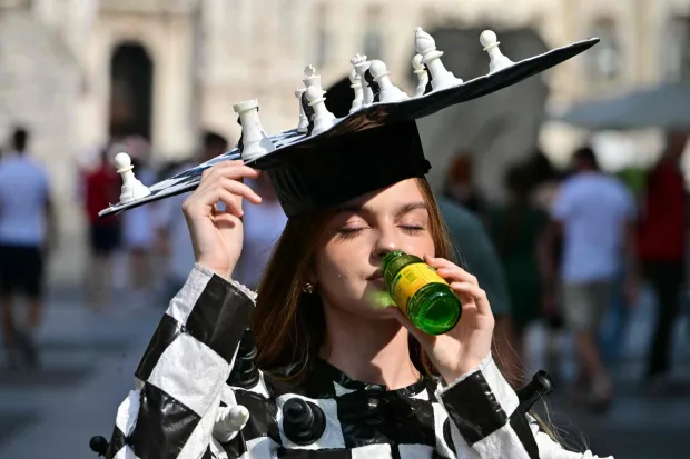 (FILES) A young woman wearing a hat resembling a chessboard drinks from a bottle at Piazza Duomo during a heatwave in Milan on June 24, 2026. To face the intensity of the record-breaking heatwave scorching Europe, people are turning to makeshift solutions to stay cool. (Photo by Stefano RELLANDINI/AFP)