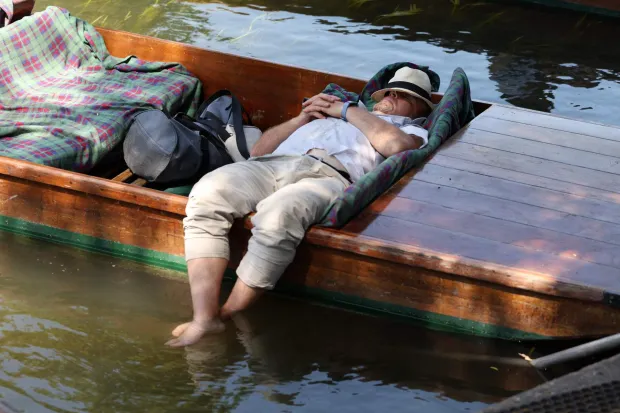 (FILES) A punt chauffer relaxes with their feet in the water between punt tours on the River Cam, during a heatwave, in Cambridge on June 24, 2026. To face the intensity of the record-breaking heatwave scorching Europe, people are turning to makeshift solutions to stay cool. (Photo by Chris RADBURN/AFP)