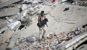 TOPSHOT - A volunteer carries a rescued dog across the rubble of a collapsed building following twin earthquakes in Caraballeda, La Guaira state, some 40 km northeast of Caracas, on June 25, 2026. The death toll from twin quakes, measured at magnitudes 7.2 and 7.5, has risen to at least 188, with more than 1,520 others injured, top lawmaker Jorge Rodriguez reported, while residents continue searching for missing relatives. (Photo by Federico PARRA/AFP)