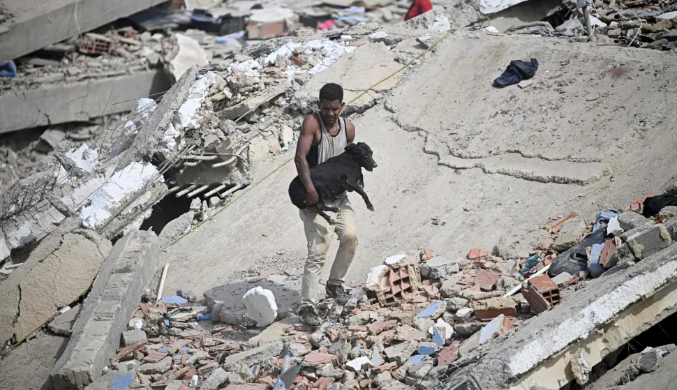 TOPSHOT - A volunteer carries a rescued dog across the rubble of a collapsed building following twin earthquakes in Caraballeda, La Guaira state, some 40 km northeast of Caracas, on June 25, 2026. The death toll from twin quakes, measured at magnitudes 7.2 and 7.5, has risen to at least 188, with more than 1,520 others injured, top lawmaker Jorge Rodriguez reported, while residents continue searching for missing relatives. (Photo by Federico PARRA/AFP)