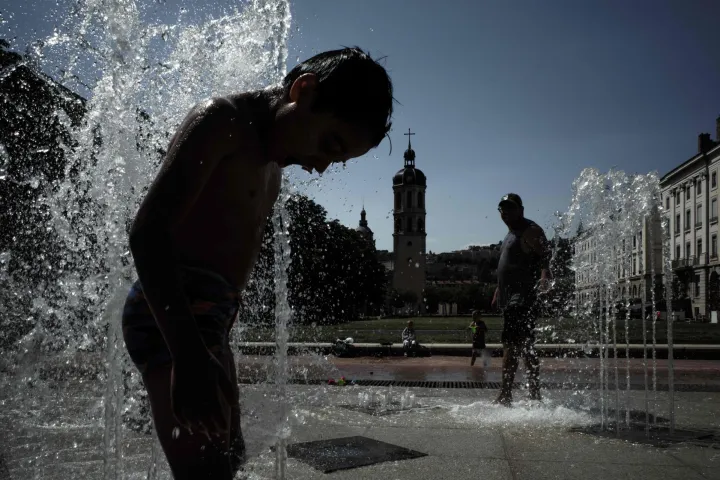 A child cools off in a fountain in Lyon on May 27, 2026 as a heatwave hits France. France is experiencing an "unprecedented" heatwave in May, with 13 departments on orange heat alert and peaks forecast at 38?39?C. National weather service Meteo France on May 26, 2026, registered a new nationwide monthly temperature record with a national heat index, which measures the average temperature across the country, of 24.8C surpassing Monday's 24.6C. (Photo by Jeff PACHOUD/AFP)