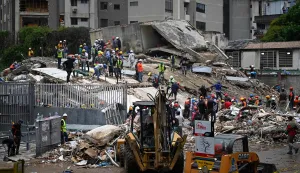 Workers remove debris from a collapsed building in the San Bernardino neighborhood of Caracas on June 28, 2026, following earthquakes. Thousands of rescuers, relatives and volunteers dig day and night through mounds of concrete to find survivors of the earthquakes that struck Venezuela more than three days ago, leaving nearly 1,500 dead and tens of thousands missing. (Photo by Federico PARRA/AFP)
