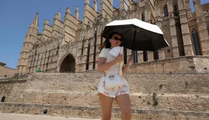 TOPSHOT - A tourist uses an umbrella as a protection against the sun as she visits Palma de Mallorca?s cathedral on June 20, 2026, on the eve of the start of the first official heatwave of this summer. Spain's first official heatwave of this summer will begin tomorrow and will last until at least June 24, 2026. The State Meteorological Agency (Aemet), the body responsible for declaring these types of episodes when they meet specific criteria regarding intensity, duration, and territorial extension, activated a special weather warning yesterday. (Photo by Jaime REINA/AFP)
