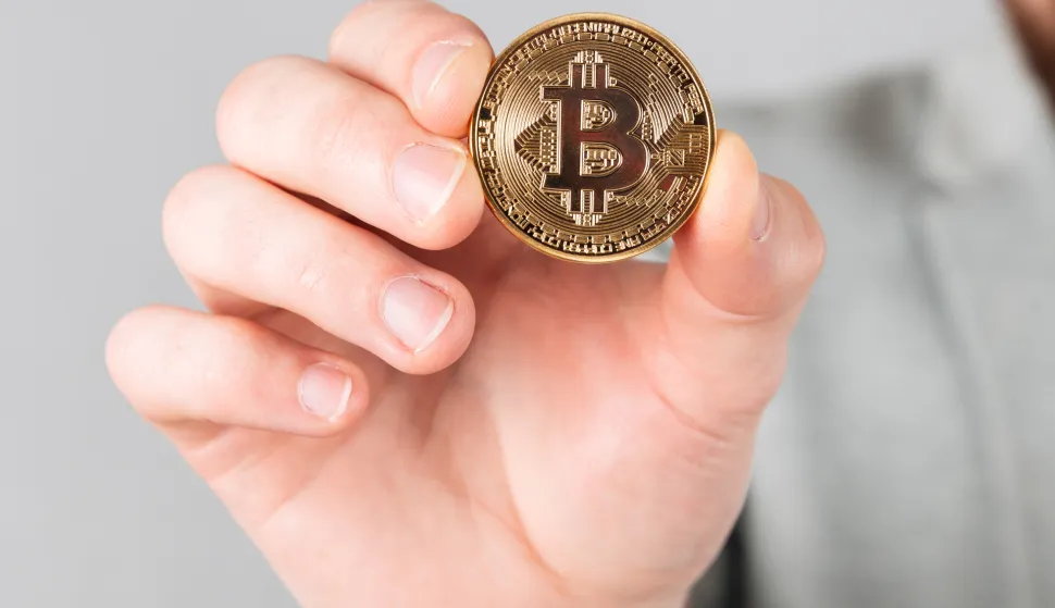 Close up of male hand showing golden bitcoin isolated over gray backgroundmagnific