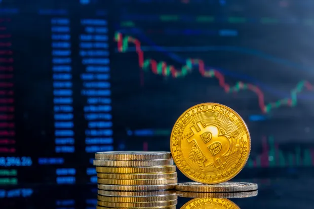 Close-up of golden Bitcoins on a dark reflective surface and the histogram of decreasing crypto in the backgroundBitcoin je lani u listopadu dosegnuo rekordnih oko 126.000 dolara, danas se njime trguje na oko 63.000 dolara. Dakle, vrijednost mu je prepolovljena. Trigeri su bili razni, a danas je to splet makroekonomskih okolnosti i strukture trži&scaron;ta. magnific