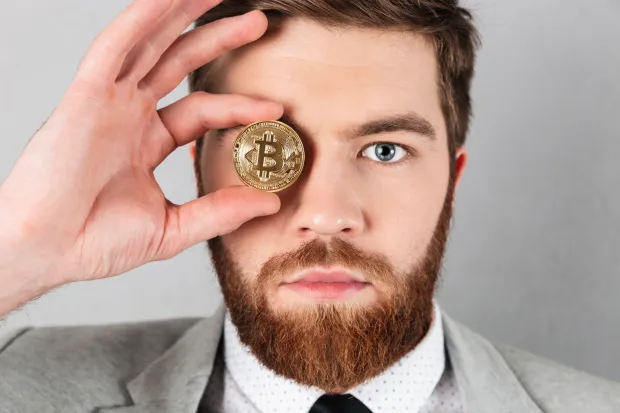 Close up of a serious businessman dressed in suit holding bitcoin at his face isolated over gray backgroundmagnific