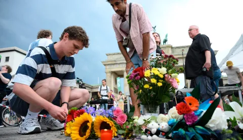 Mourners place bouquets of flowers on July 26, 2026 in front of landmark Brandenburg Gate during to a so-called "community mourning" one day after the car ramming attack on people on the outskirts of Berlin's Christopher Street Day (CSD) parade on late July 25, 2026, killing one person and injuring 16 in the Tiergarten park. German police searched on July 26, 2026 for a suspect believed linked to Islamist circles after a car ploughed into a crowd near Berlin's Gay Pride celebrations, killing one person and wounding 16 others. The incident shattered what had been a day of celebration for hundreds of thousands attending Christopher Street Day, one of Europe's largest Pride events, and left revellers fleeing a central Berlin park as sirens echoed through the night. (Photo by RALF HIRSCHBERGER/AFP)