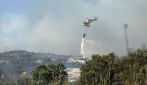 A firefighter helicopter dumping water is pictured as a fire started in an industrial area of San Martin de Valdeiglesias, about 70km west of Madrid, on July 26, 2026. In the western Madrid region, two separate wildfires merged on July 24 into a massive blaze that nearly joined another fire in neighboring Castile and Leon. The flames have already burned 25,000 hectares across Madrid and neighboring Avila province, forcing more than 60,000 people to flee their homes, according to authorities, who labeled the fire the "worst in history" for the Madrid region. (Photo by Oscar DEL POZO/AFP)