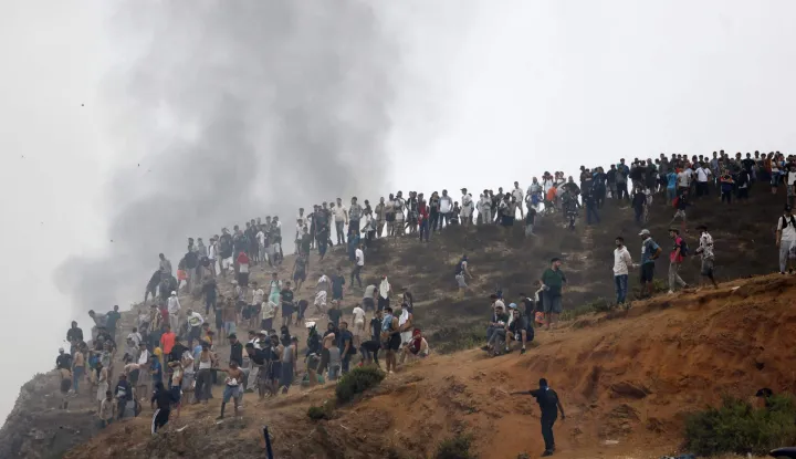 TOPSHOT - People gather on a hilltop as smoke billows from the site of clashes near Fnideq, on the Morocco-Spain border, on July 31, 2026. Thousands of migrants crossed overnight from Morocco into Spain's north Africa's Ceuta enclave, a police source said on July 31, adding that it was impossible to estimate how many people in total. A total of 18 people died while attempting to reach the Spanish enclave, the source said. (Photo by Abdel Majid BZIOUAT/AFP)