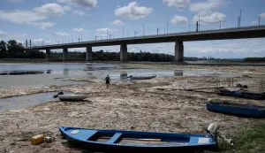A fisherman tries to move his boat, blocked by algae on the bottom of the Danube river in front of the Calafat-Vidin bridge, connecting Bulgaria and Romania near the village Antimovo, southeastern Bulgaria, on July 22, 2026. At the Romanian town of Corabia on the banks of the Danube river, some boats are stranded in shallow water full of algae in the touristic port, which lies deserted as ships can no longer dock due to sandbars (Photo by Nikolay DOYCHINOV/AFP)
